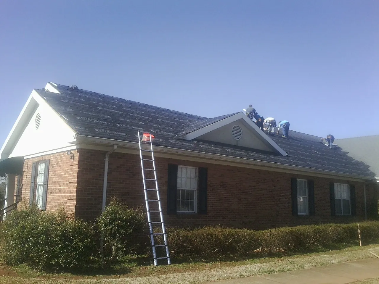 Crew tearing shingles off a brick ranch roof with a ladder set — Metal Roof Repair work by our crew in Elverta