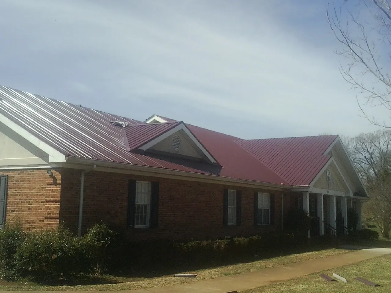 Red metal roof with gabled entries on a long brick building, from a Hail Damage Roof Repair job in Elverta