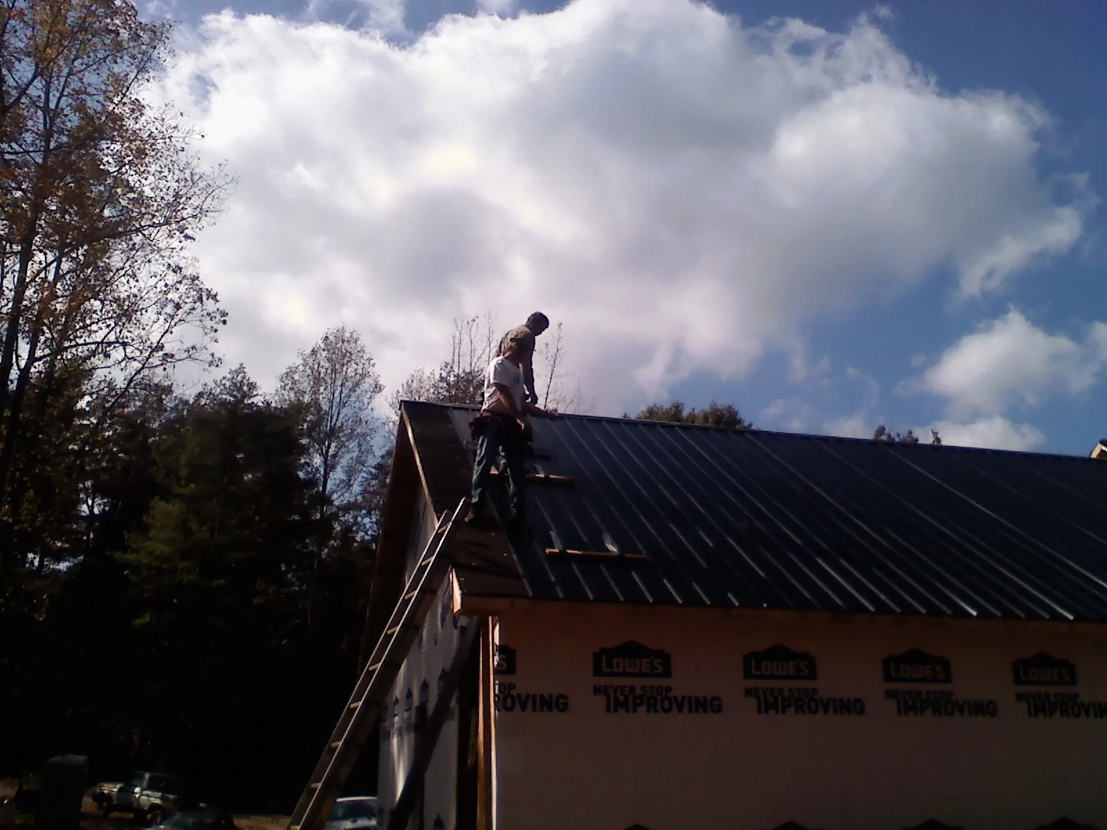 Roofer fastening dark metal panels high against a cloudy sky, from a Roof Inspection job in Elverta
