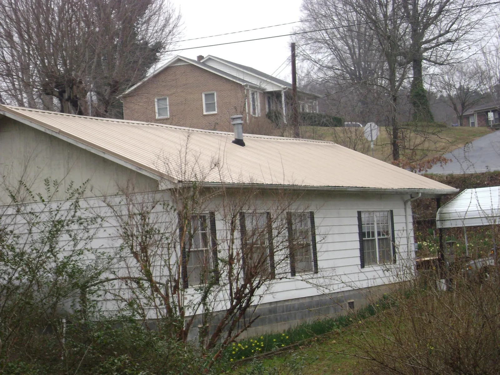 Tan metal roof on a white sided house set into a hillside — Commercial Roofing by Roofing Brothers in Elverta